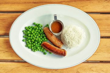 Fried Sausages with green pea, sauce and rice on a plate, wood table background, Top view, close up