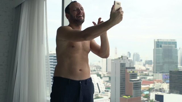 Topless man taking selfie photo with cellphone by window at home, super slow motion 240fps

