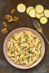 Penne pasta with zucchini and ham stripes and walnut served on plate, photographed overhead on slate with natural light
