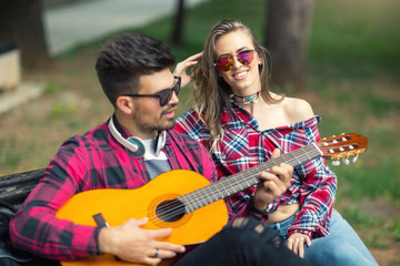 Fototapeta na wymiar Happy Couple at the Park Playing Guitar and Singing Songs.