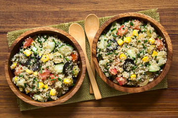 Quinoa salad with sweet corn, olive, tomato, cucumber and chives in wooden bowl, photographed overhead on dark wood with natural light (Selective Focus, Focus on the top of the salad)