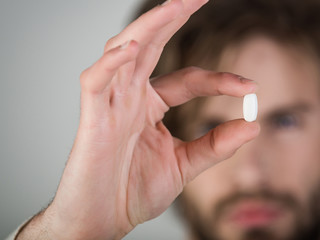 Capsule, drug or pill in the hand of young blurred man. Male hand holding pill. Young Bearded Man Holding white Color Pill. Medicine Health Care People Concept. Closeup man face taking white pill