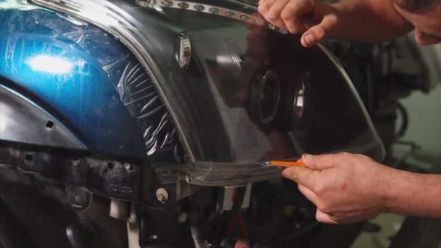 Close up shot of the hands of man who cut the vinyl film on the headlights of blue expensive car. This film protects the vehicle from the small chips and scratches.