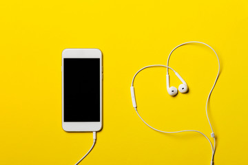 Close-up of smart phone with headphones on a yellow background. (Top view). Listen to music.