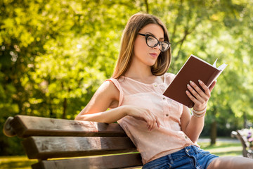 Young woman sitting on a bench in the park and reading book