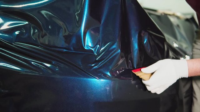 Close up shot of expert's hands with white gloves in the service station put vinyl on the machine. Employees salon carefully glued a blue film on the expensive car.
