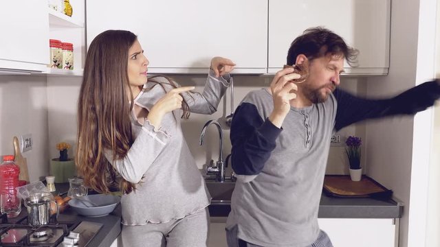Woman looking crazy boyfriend dancing while eating donut in kitchen