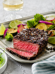 Grilled pepper steak garnished with lemon, onion and fresh herbs