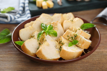 Plate with slices of tasty garlic bread on wooden table