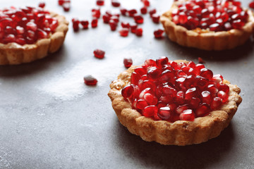 Tasty tarts with fresh seeds of pomegranates on gray table