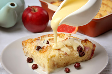 Pouring sauce on tasty bread pudding with berries on table