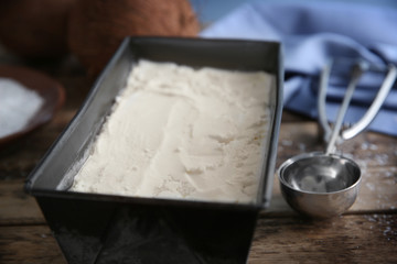 Black container with fresh coconut ice cream on wooden table