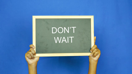 boys hand holding a blackboard with the words " DON'T WAIT"