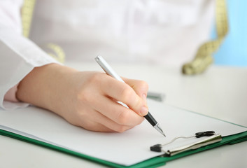 Young female nutritionist writing diet plan, closeup