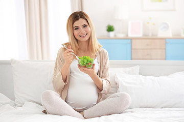 Obraz na płótnie Canvas Young pregnant woman having breakfast while sitting on bed at home