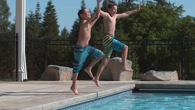 Two boys jumping into pool in super slow motion