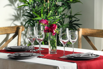 Beautiful festive table setting and vase with flowers in light room