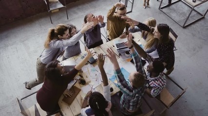 Top view of business team working at trendy loft office. Young mixed race group of people puts palm together on centre. - Powered by Adobe