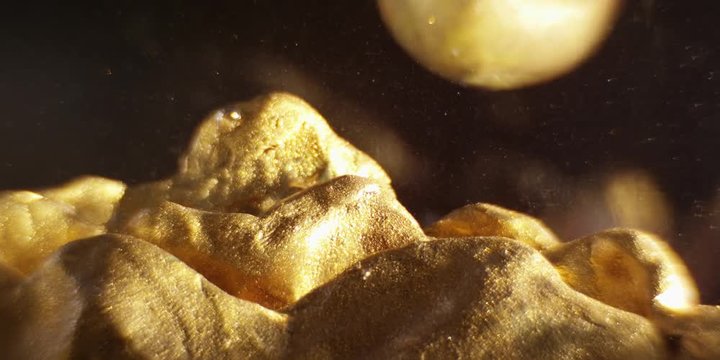 Abstract models mountains and planet made of golden plasticine, immersed in liquid. Closeup. 4K. Camera RED.
