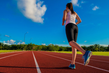 Sporty woman running on stadium track in evening closeup on sport wear, shoes and legs . Fitness and workout wellness concept.