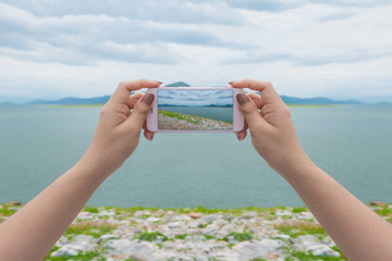 Taking photo on mobile phone concept. Hand holding mobile smart phone with lake view.