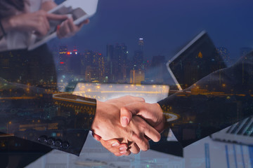 Double Exposure of a businessman handshake on Aerial view of a city skylines and the highway heading into the city at night.