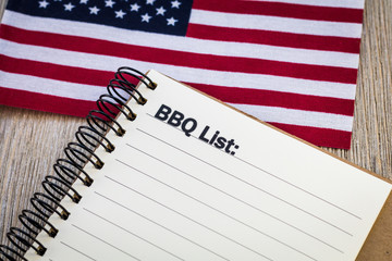 BBQ list concept on notebook and wooden board with USA flag for a patriotic theme