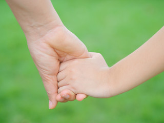 Mother holding a hand of her kid in spring day outdoors with green field background