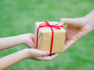 holidays, present, christmas, childhood and happiness concept - close up of child and mother hands with gift box over green background