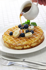 pouring maple syrup over homemade american round waffles
