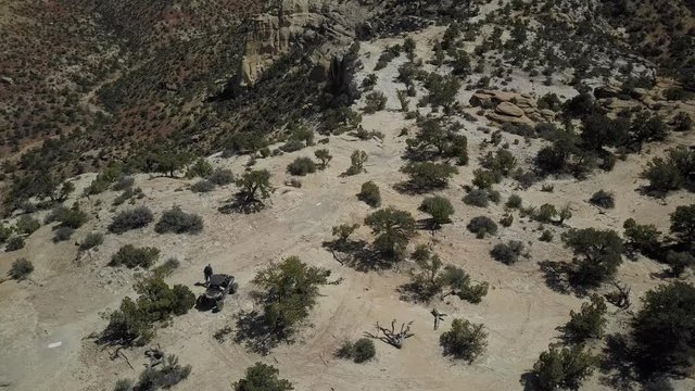 Aerial circle off road recreation man walking desert cliff. Geologic desert landscape. Erosion rock towers, cliffs, and deep canyons. 4x4 all terrain off road vehicle. Dangerous wilderness.