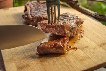 Sliced Grilled Beef Steaks On Wooden Board with knife and fork