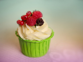 Cupcake with cream cheese frosting decorated with raspberry and redcurrant on top over colorful background. Sweet dessert. Shallow DOF. Selective focus on the raspberry.