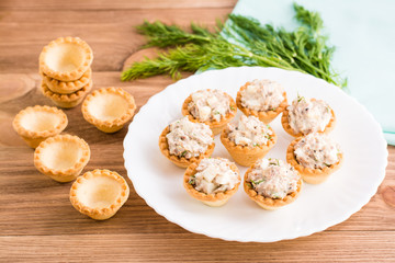 Тарталетки с салатом из сайры и яиц на тарелке и пустые тарталетки на столе