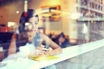 Cafe city lifestyle woman on phone drinking coffee texting text message on smartphone app sitting indoor in trendy urban cafe. Cool young modern mixed race Asian Caucasian female model in her 20s.