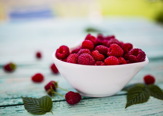 Fresh raspberries in heart shape bowl on wooden table in the garden.