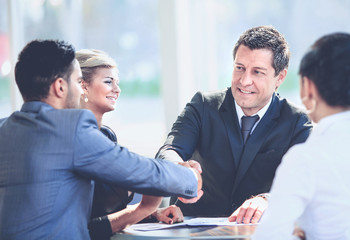 Mature businessman shaking hands to seal a deal with his partner and colleagues in a modern office