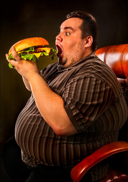 Diet failure of fat man eating fast food hamberger. Happy smile overweight person who spoiled healthy food by eating huge hamburger on fork. Junk meal leads to obesity. Very fat man eating