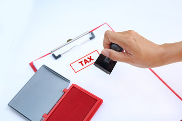 Close-up hand Stamping Tax on paper sheet with red Ink pad(box) against white background.


