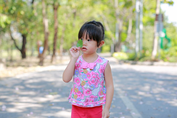 Portrait of cute little girl in the public park with funny face and posture with green leaf