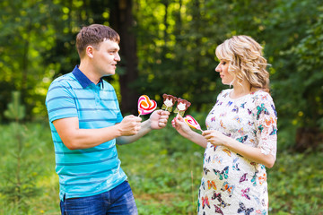 Pregnancy, family, happiness and fun concept - Man and pregnant woman have fun with candy in the park