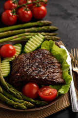 Grilled beefsteak with asparagus and vegetables on black background.