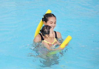 Happy smiling asian little girl with mother learning to swim with pool noodle