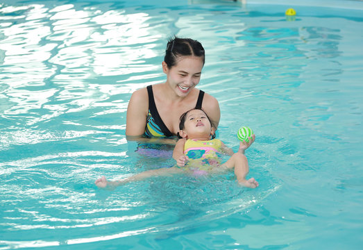 Mother and child swimming in the pool. Happy young woman teaching her daughter to swim.