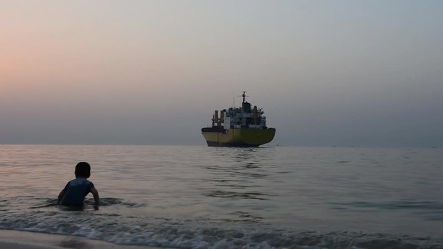 Boy Playing in the Beach at evening time and cargo ship in background