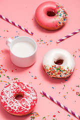 Donuts with icing and milk on pastel pink background. Sweet donuts.
