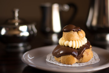 Closeup of a Chocolate cream puff pastry with a silver set of coffee and milk