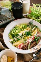 Traditional Russian summer Cold Soup Okroshka with kefir and kvass serving size in bowl and ingredients on wooden table