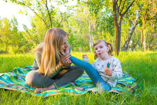 Young mother with her amusing daughter relaxing in a park