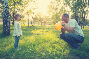 Happy father and smiling little daughter are blowing colored balloons